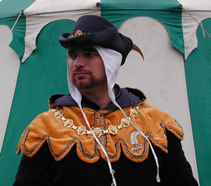 Gold 'U' Dagged Velvet Hood and Liripipe with Dark Blue Brocade Lining, trimmed with Blue and Gold Braid and 'watchet' coloured Jewelled buttons centre front